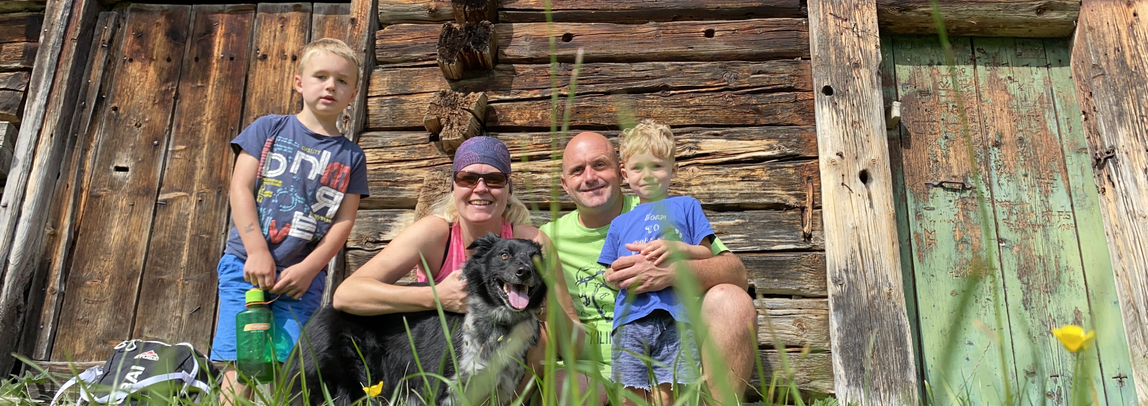 Eine Familie mit zwei Kindern und Hund sitzt vor einer rustikalen Holzhütte im Grünen in Lofer.