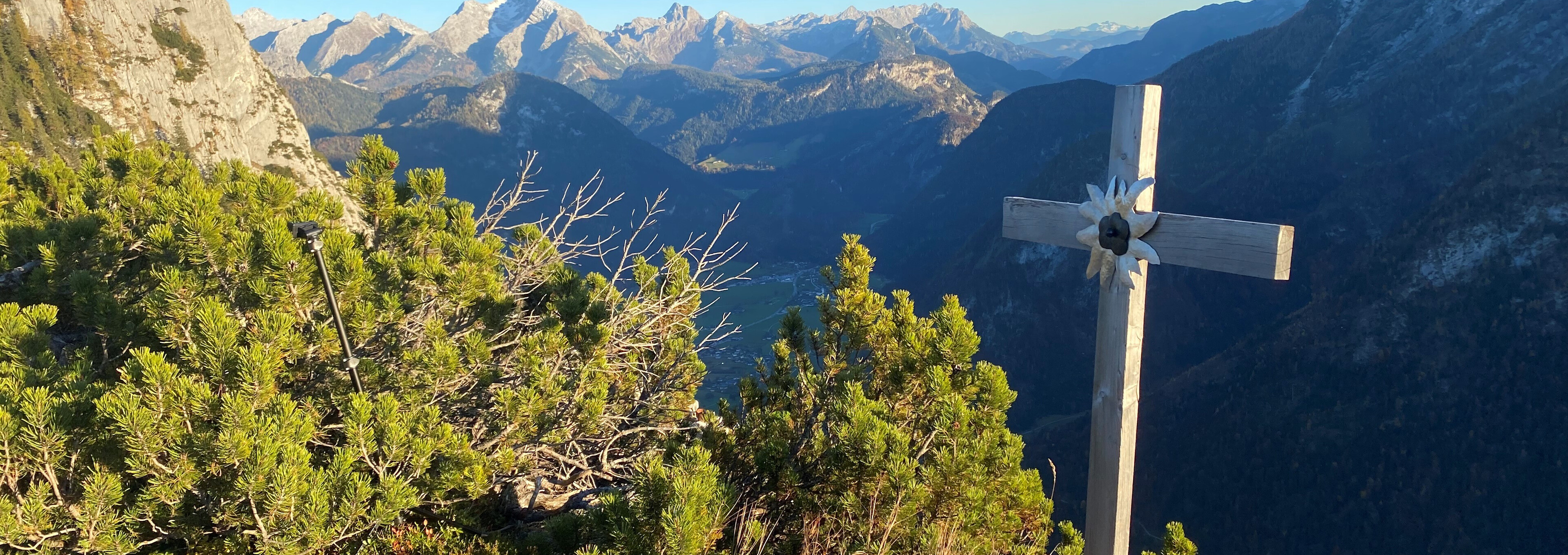 Holzgipfelkreuz auf dem Urlkopf mit Panoramablick auf die Saalachtaler Alpen im Sonnenschein.