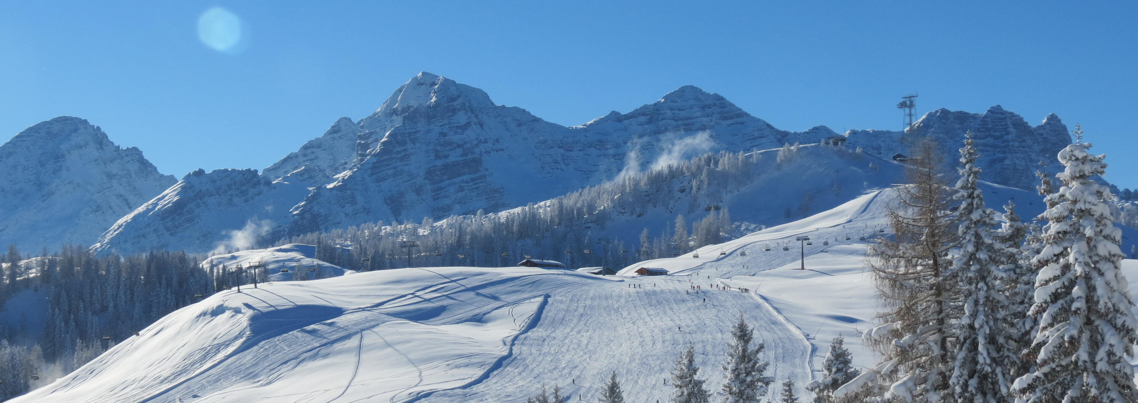 Verschneite Pisten und Bergspitzen der Almenwelt Lofer im Saalachtal an einem sonnigen Wintertag.