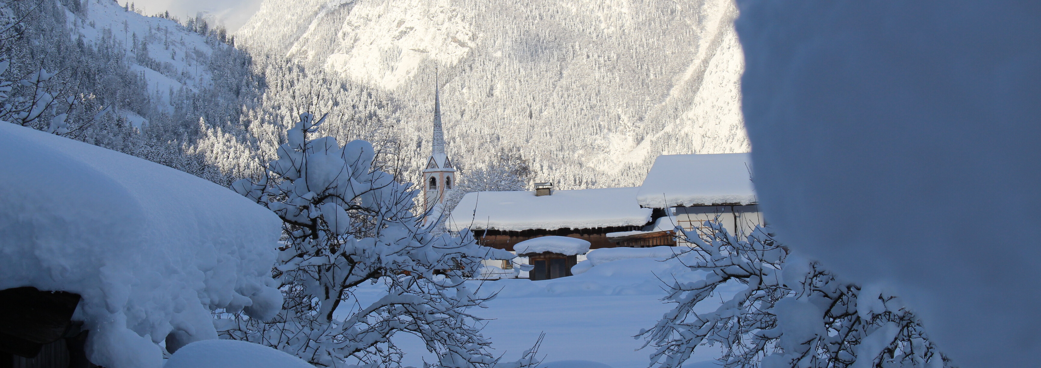 Tief verschneite Winterlandschaft in St. Martin bei Lofer mit Blick auf den Kirchturm und die Berge.
