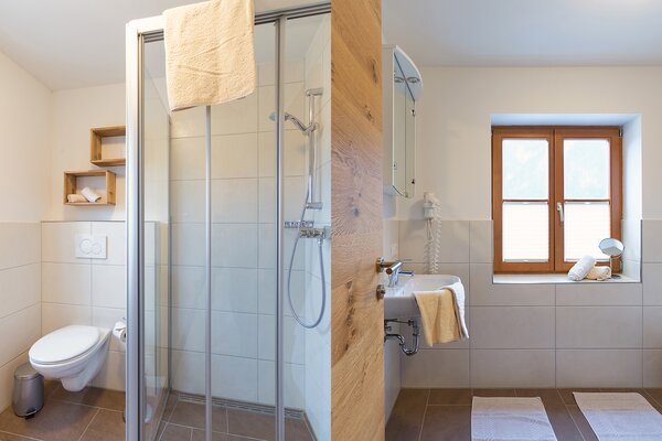 Modernes Badezimmer der Ferienwohnung Breithorn mit Glasdusche, WC und Holzfenster in St. Martin bei Lofer.