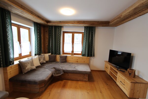 Gemütliches Wohnzimmer der Ferienwohnung Eiblhorn mit Holzelementen, Eckcouch und Fernseher in Lofer.