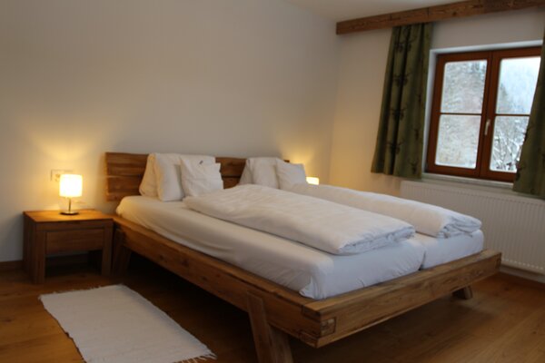 Gemütliches Schlafzimmer der Ferienwohnung Eiblhorn mit massivem Doppelbett aus Holz und Nachttisch.