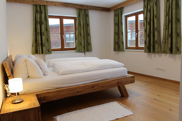 Gemütliches Schlafzimmer der Ferienwohnung Eiblhorn mit Massivholzbett und grünen Vorhängen in Lofer.
