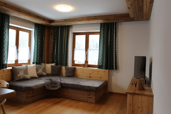 Gemütliches Wohnzimmer der Ferienwohnung Eiblhorn mit Eckcouch, Fernseher und edlem Holzdesign in Lofer.