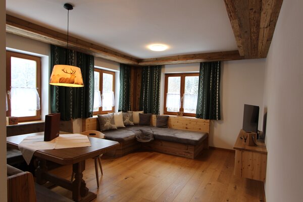 Gemütliches Wohnzimmer der Ferienwohnung Eiblhorn mit Essecke, Eckcouch und Altholz-Elementen in Lofer.