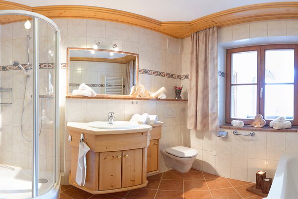 Geräumiges Badezimmer der Ferienwohnung Ochsenhorn mit Glasdusche, Badewanne und Holzwaschtisch.