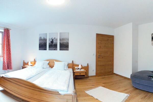 Geräumiges Schlafzimmer der Ferienwohnung Ochsenhorn mit Doppelbett aus Holz und blauer Recamiere in Lofer.