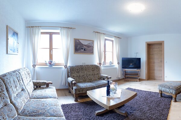 Gemütliches Wohnzimmer der Ferienwohnung Ochsenhorn mit Couchgarnitur, Fernseher und Holzboden.