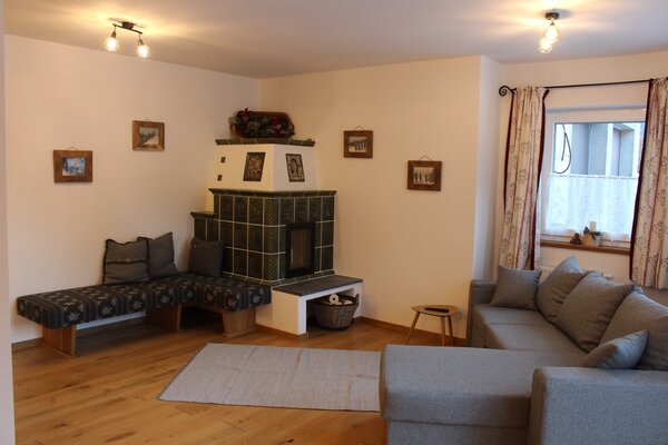 Gemütlicher Wohnraum der Ferienwohnung Schihörndl mit großem Sofa und traditionellem Kachelofen in Lofer.