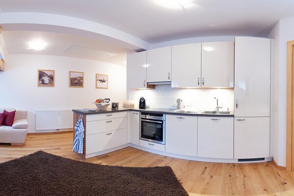 Offene weiße Küche und Wohnbereich der Ferienwohnung Vorderhorn mit Holzboden in St. Martin bei Lofer.