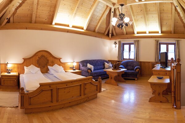 Gemütliches Schlafzimmer der Ferienwohnung Vorderhorn mit Doppelbett, Couch und hoher Holzdecke in Lofer.